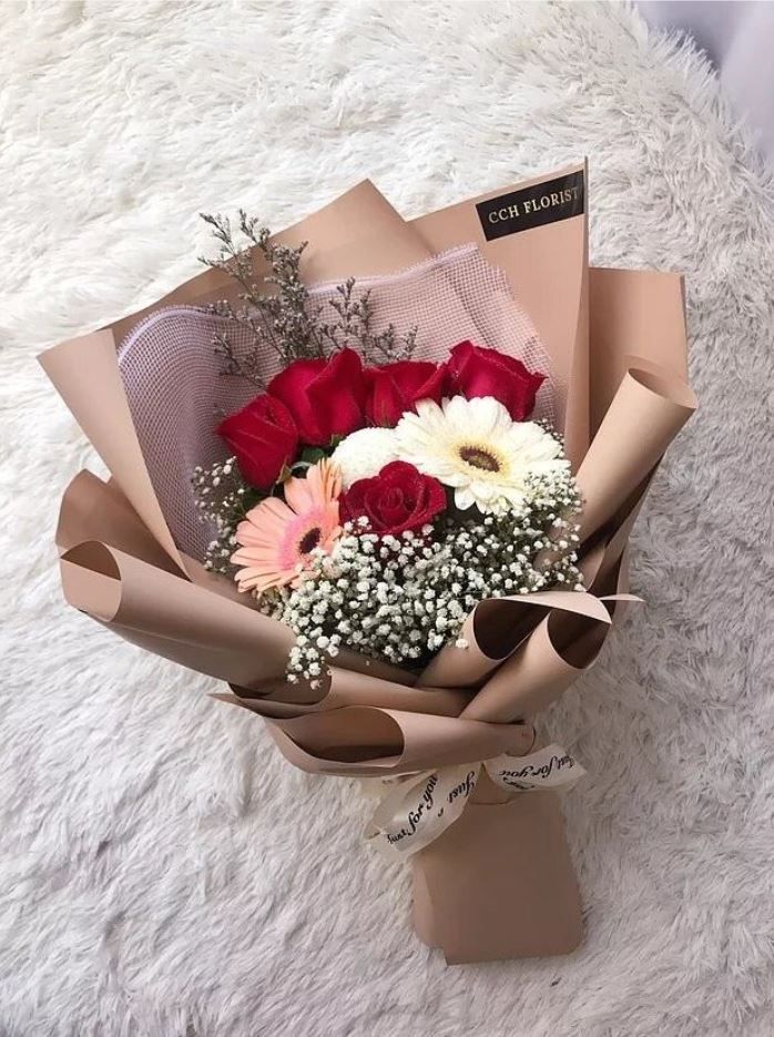 a bouquet of roses and baby's breath wrapped in brown paper on a white rug