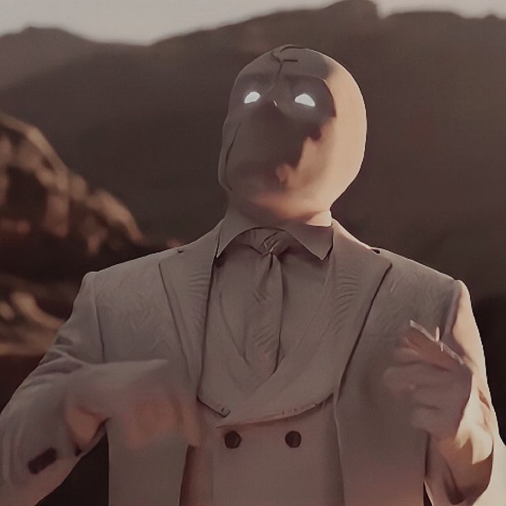 a man wearing a suit and tie with his hands out to the side, in front of mountains