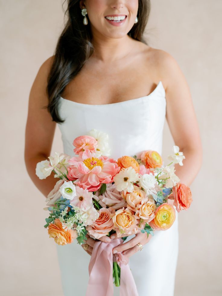 a woman holding a bouquet of flowers in her hands and smiling at the camera while wearing a white strapless dress