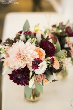 a vase filled with lots of flowers on top of a white table covered in greenery