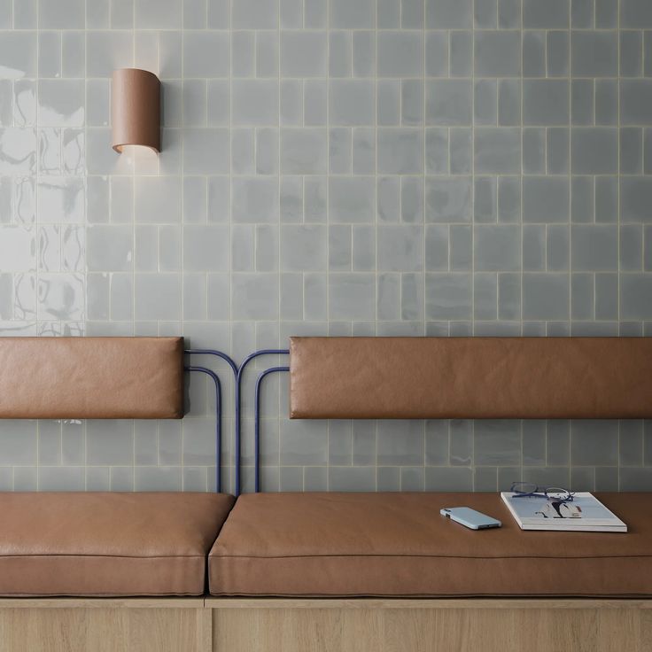 two brown benches sitting next to each other in front of a wall with white tiles