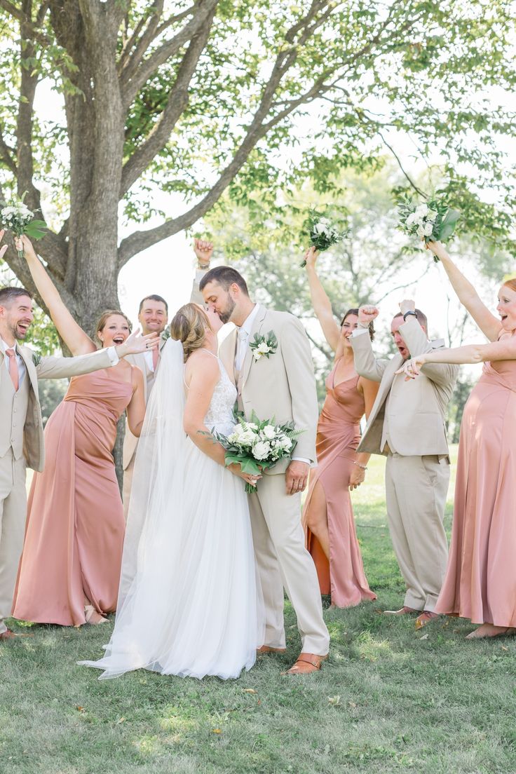 a bride and groom with their bridal party in front of a tree at the park