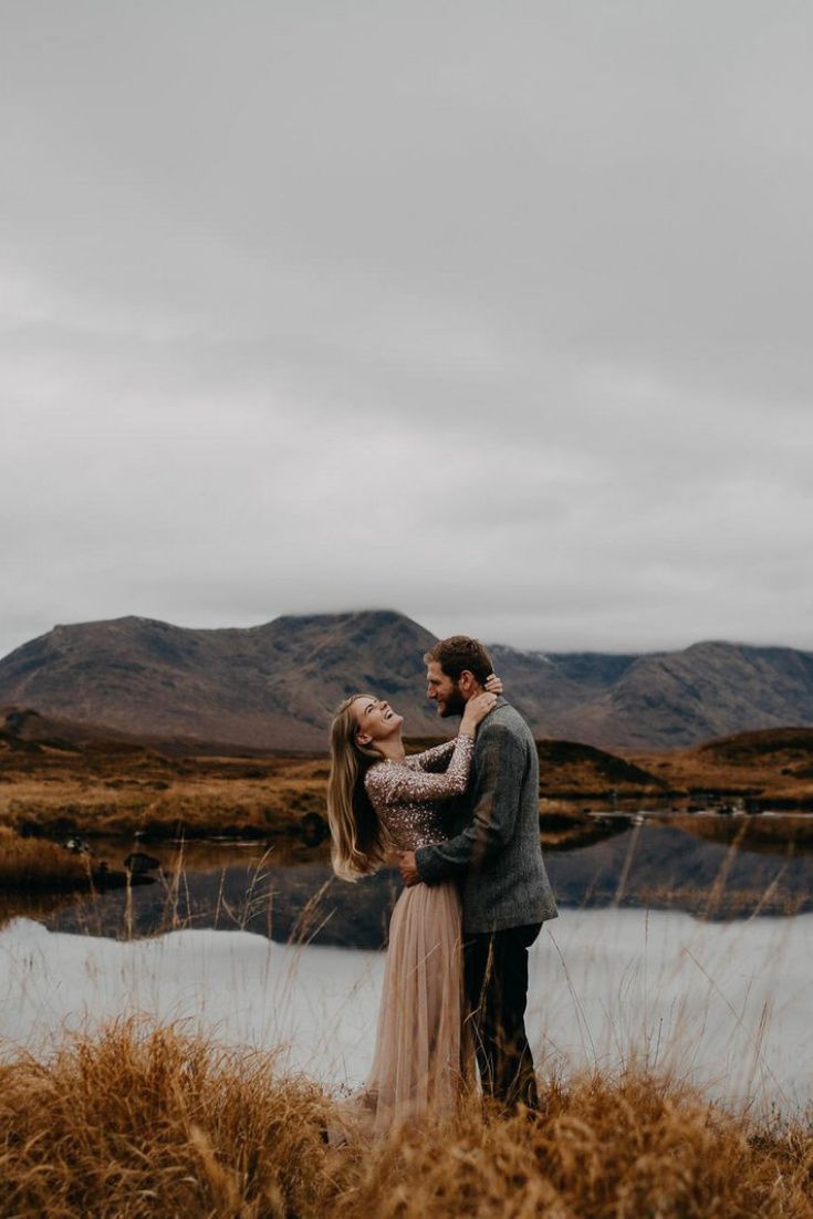 a man and woman standing next to each other in front of a body of water