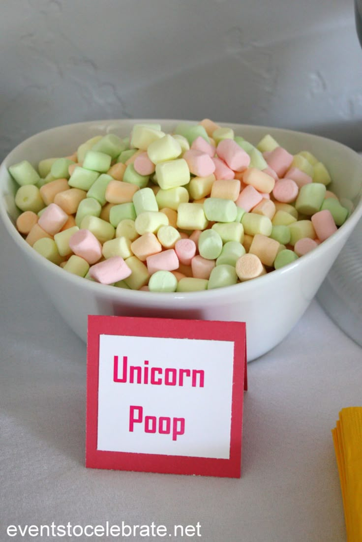 a bowl filled with candy corn sitting on top of a table next to a sign that says unicorn poop