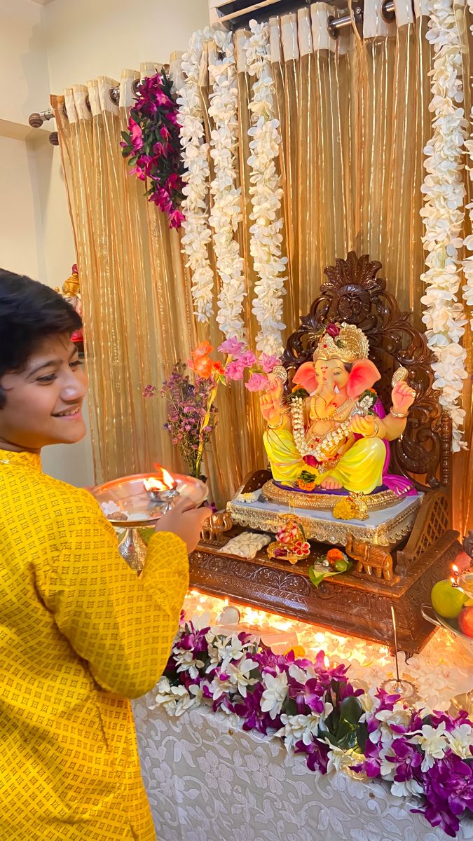 a woman is lighting candles in front of a decorated ganeshi idol with flowers and garlands