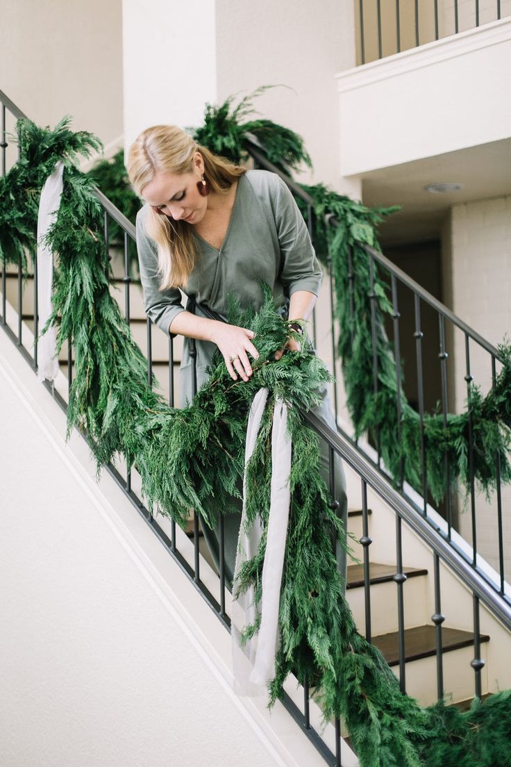 a woman is walking down the stairs decorated with christmas garlands and pine cones for holiday decor