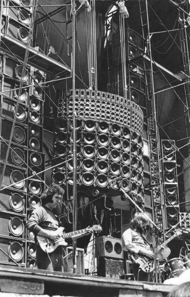 black and white photograph of people playing instruments on stage in front of a large structure