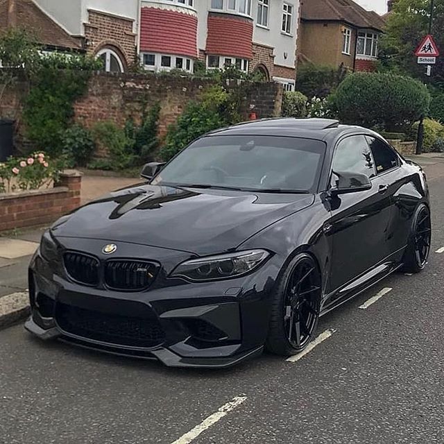 a black bmw is parked on the side of the road in front of some houses