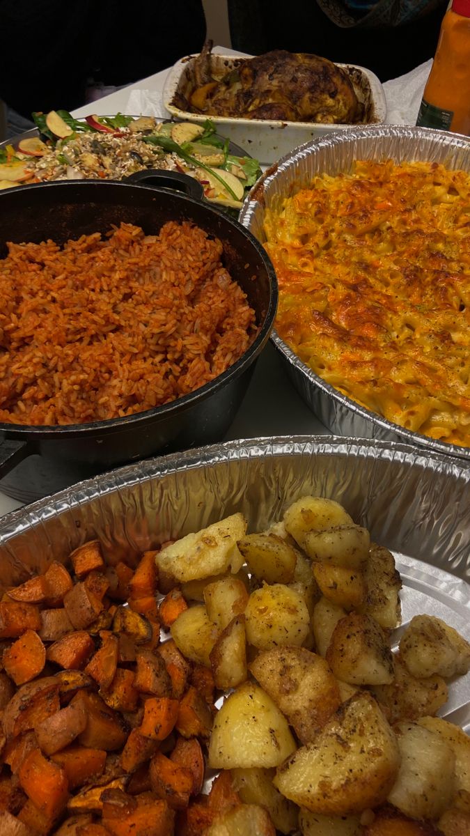 there are many different types of food in tin foil pans on the table, including potatoes and carrots