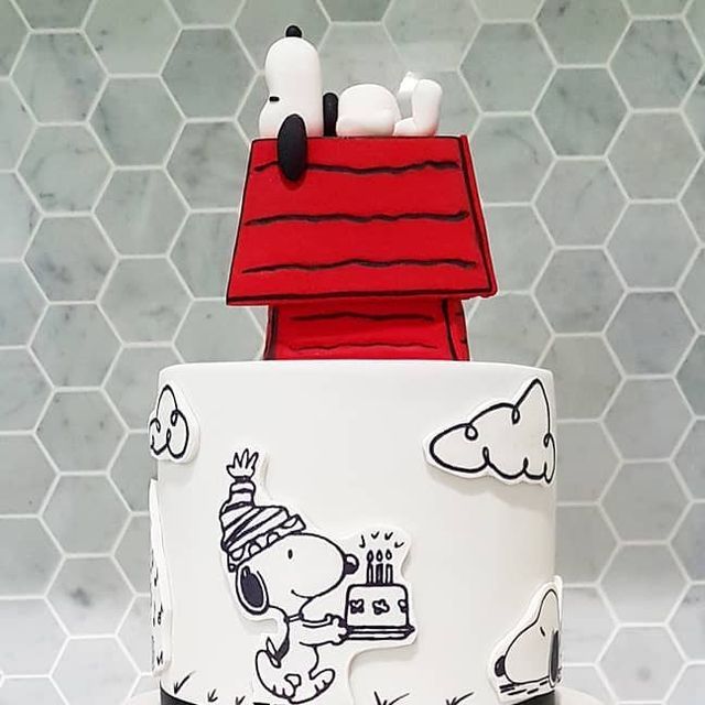 a three tiered cake decorated with peanuts and snoopy on the top, sitting on a table