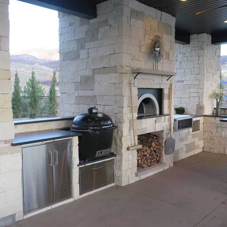 an outdoor kitchen with stone fireplace and grilling area next to large open patio doors