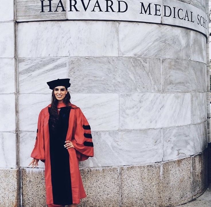 a woman standing in front of a building wearing a graduation gown and holding a book