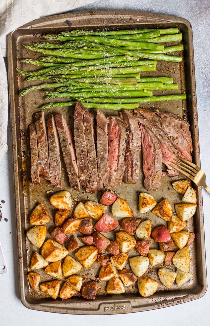 steak, potatoes and asparagus on a baking sheet with a fork next to it