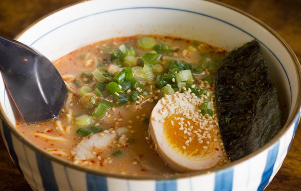 a bowl of soup with an egg and some sort of meat in it on a wooden table