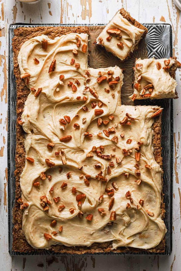 carrot cake with frosting and walnuts on a baking sheet next to a cup of coffee