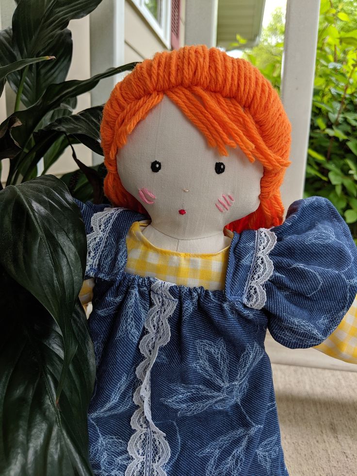 a doll with orange hair is sitting next to a potted plant