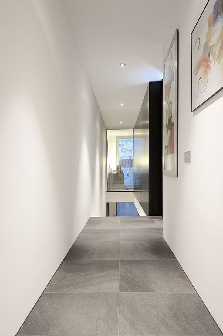 an empty hallway with white walls and grey flooring is seen in this image, there are two framed pictures on the wall