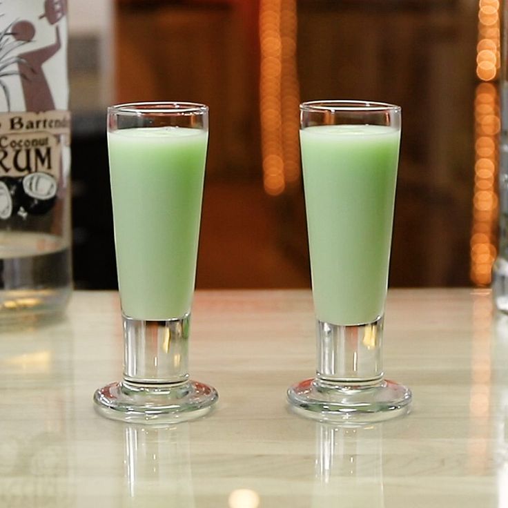 two glasses filled with green liquid sitting on top of a counter