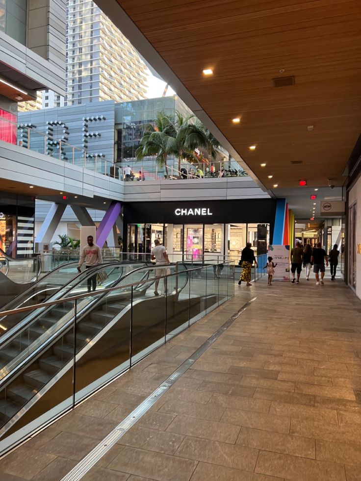 people are walking down an escalator in a shopping mall with glass railings