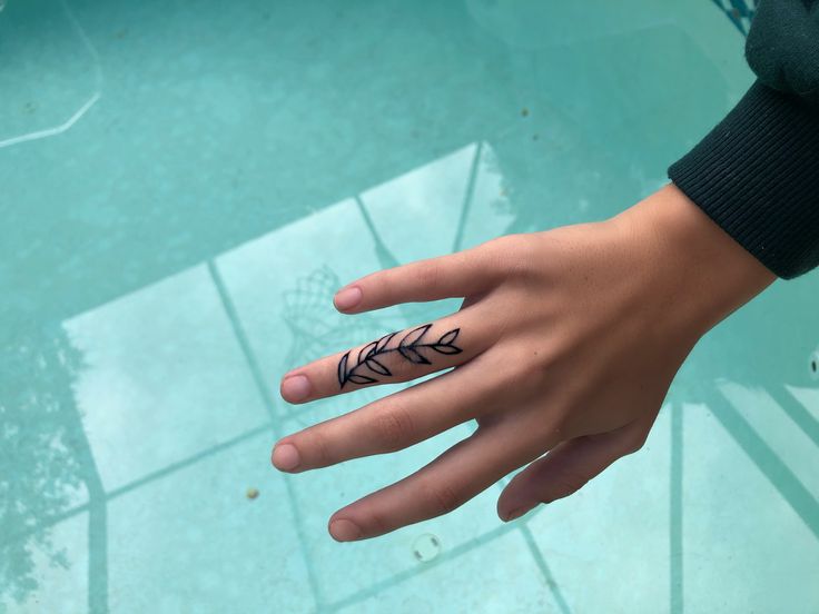 a person's hand with an arrow tattoo on the middle of their finger, near a swimming pool