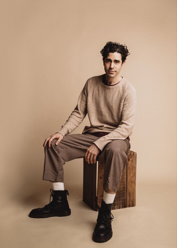 a man sitting on top of a wooden box wearing black shoes and a tan sweater