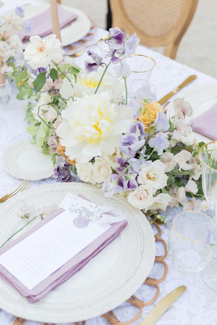 the table is set with purple and white flowers, napkins, and place settings