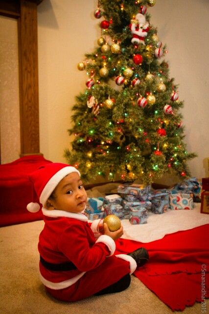 a baby sitting on the floor in front of a christmas tree