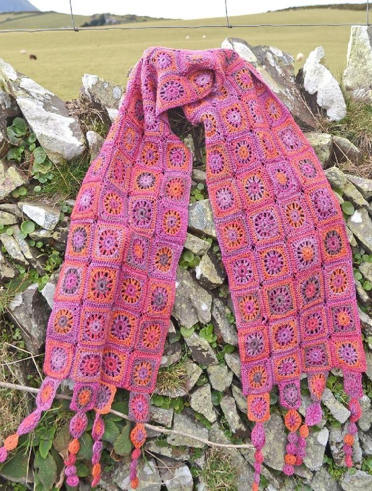 a pink crocheted scarf sitting on top of a pile of rocks next to a field