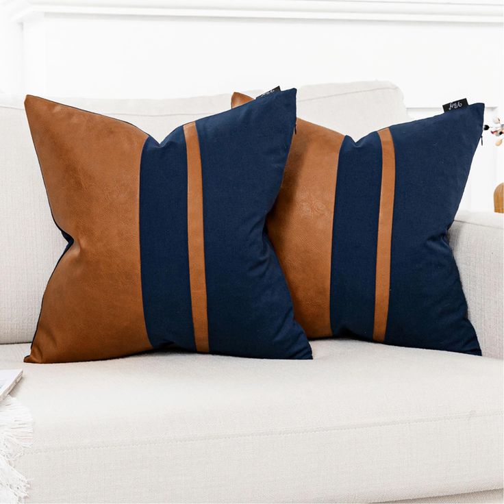 two brown and blue pillows sitting on top of a white couch next to each other