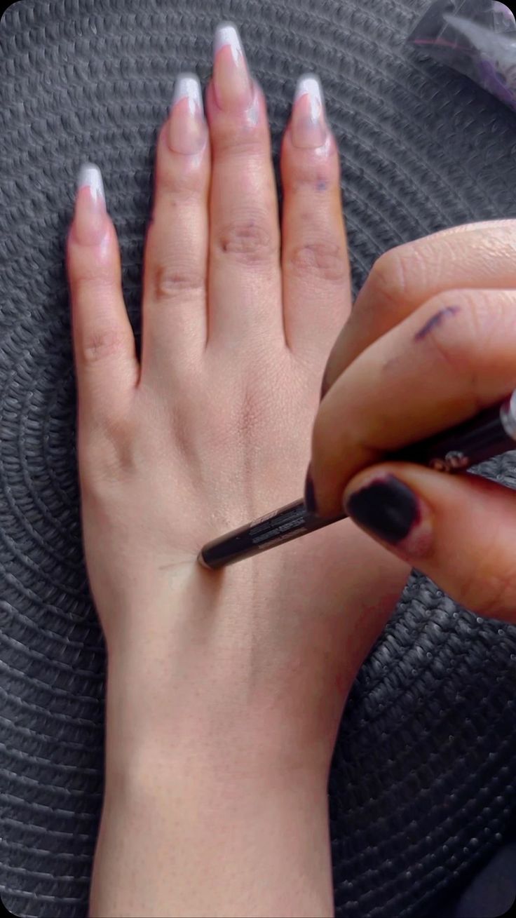 a woman's hand with white and black nail polish on her nails holding a pen