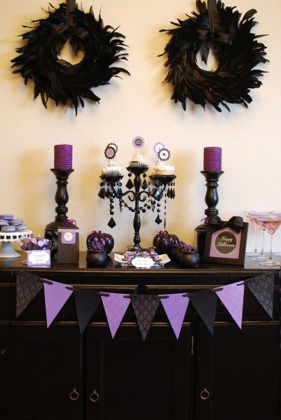 a table topped with purple and black desserts next to tall candle holders on top of a dresser