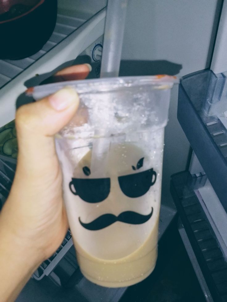 a person holding up a plastic cup with a mustache on it