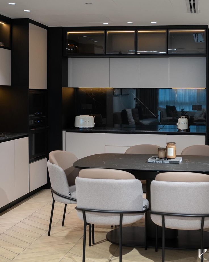 a dining room table surrounded by chairs in front of a kitchen with black and white cabinets