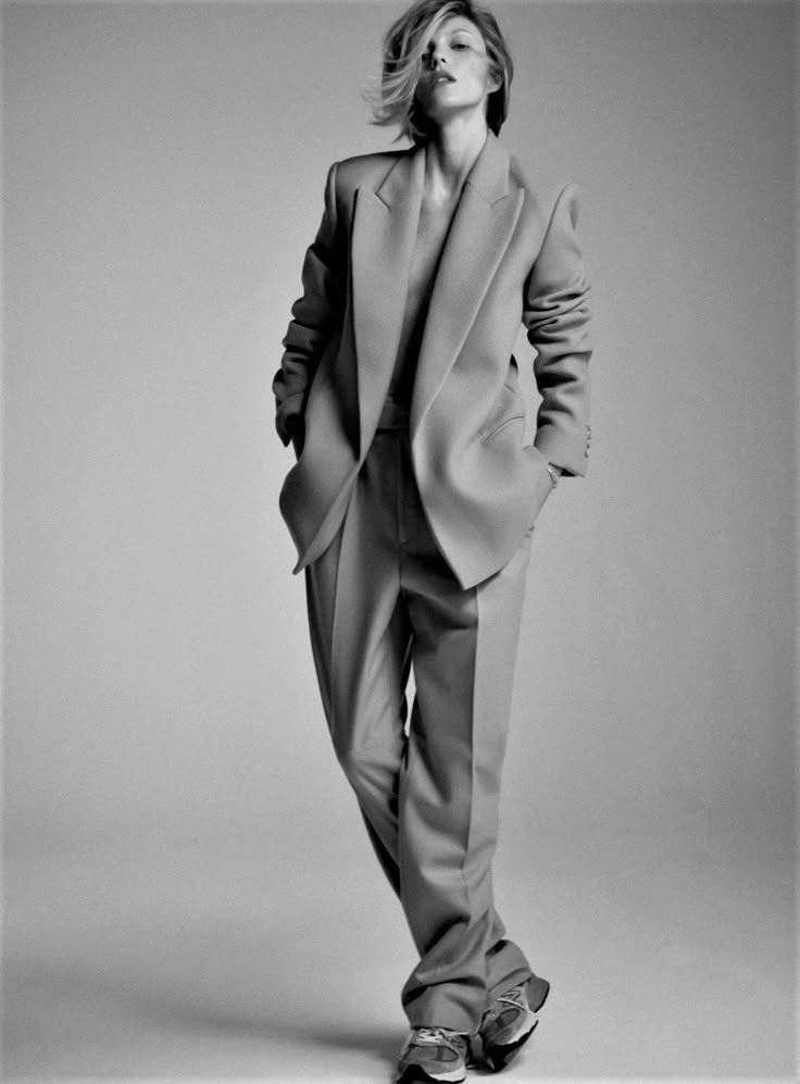 a black and white photo of a woman in a suit standing with her hands on her hips