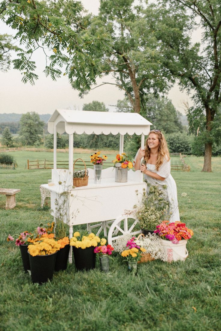 a woman standing next to a white cart filled with flowers