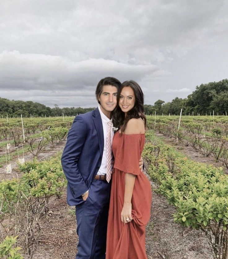 a man and woman posing for a picture in front of some vines at a winery