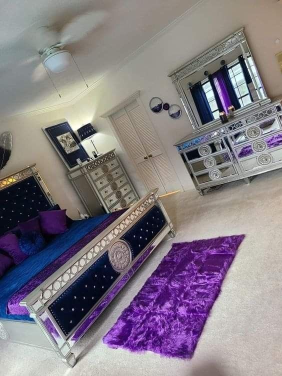 a bedroom with purple and blue decor on the bed, dressers and mirror in the corner