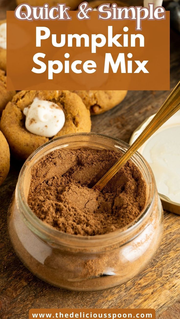 pumpkin spice mix in a glass jar with spoon and cookies on the table behind it