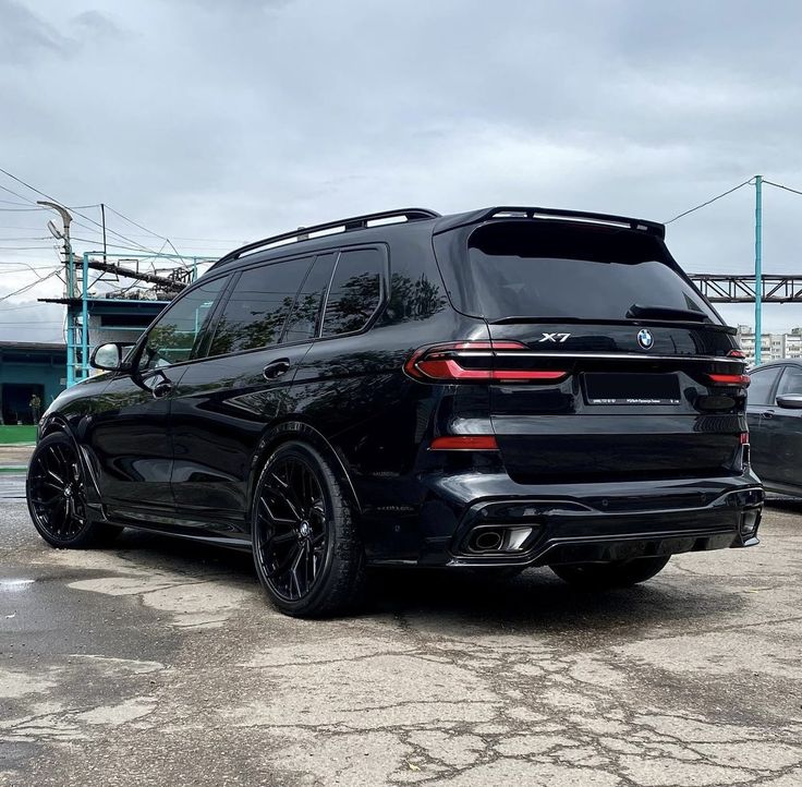 the rear end of a black bmw suv parked in a parking lot next to other cars