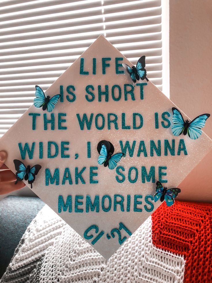 a white graduation cap with blue butterflies on it that says life is short the world is wide, i wanna make some memories