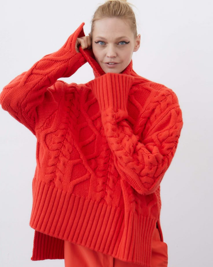 a woman in an orange sweater poses for the camera with her hand on her head