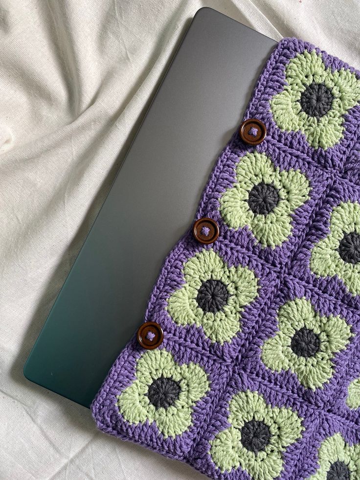 a laptop computer sitting on top of a purple and green crocheted cover with flowers