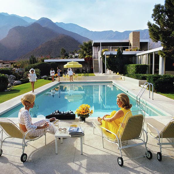 two women sitting in lawn chairs next to a swimming pool with mountains in the background