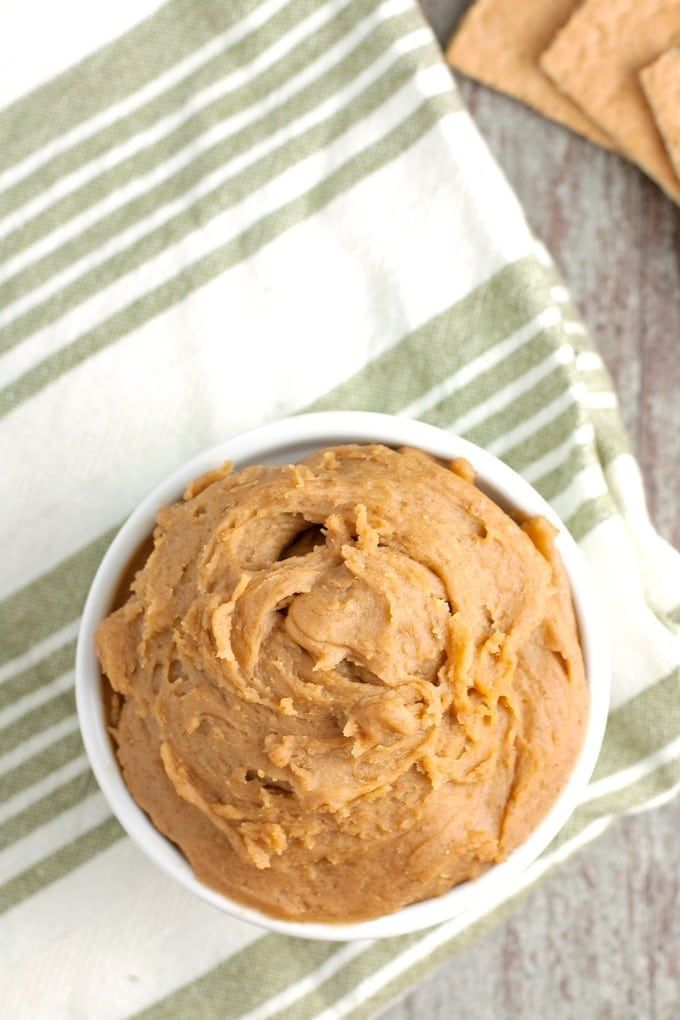 a white bowl filled with peanut butter next to crackers on a green and white towel