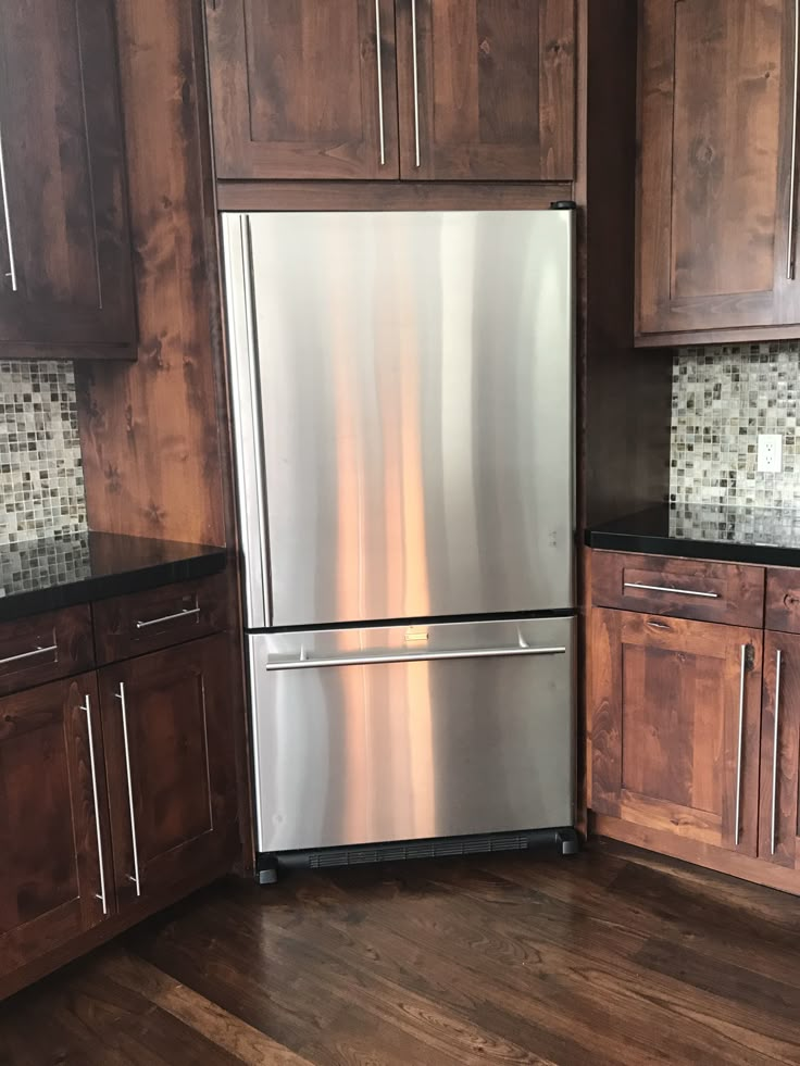 a stainless steel refrigerator in a kitchen with wooden cabinets and wood flooring on the walls