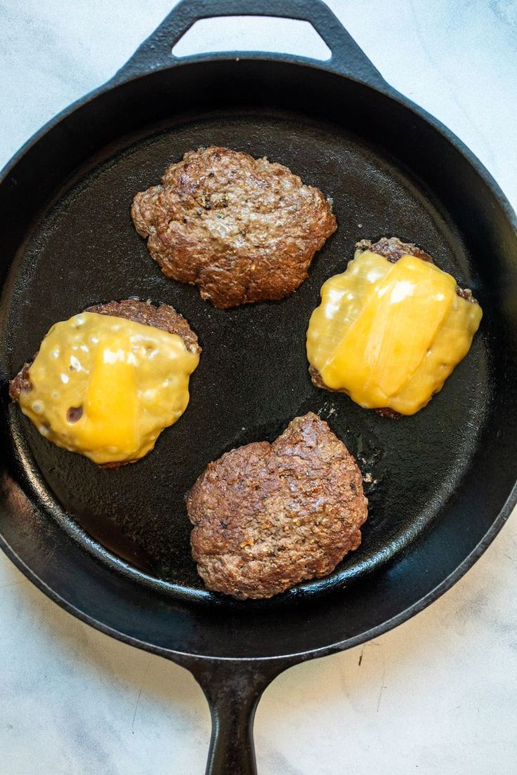 three hamburger patties are being cooked in a cast iron skillet with yellow sauce