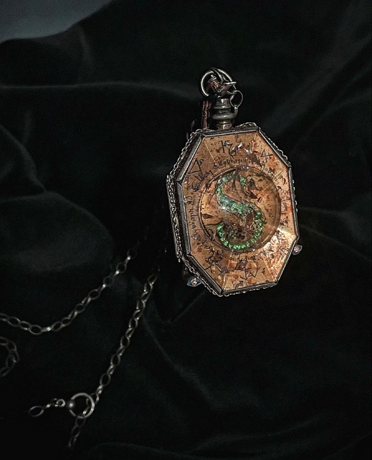 an antique pocket watch with a green dragon on it's face is sitting on a black cloth