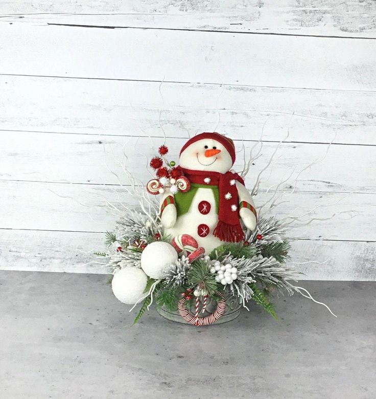 a snowman sitting on top of a bowl filled with christmas decorations and greenery