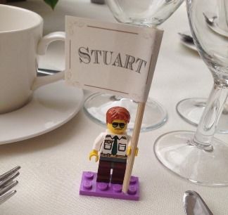 a lego man holding a sign sitting on top of a table next to wine glasses