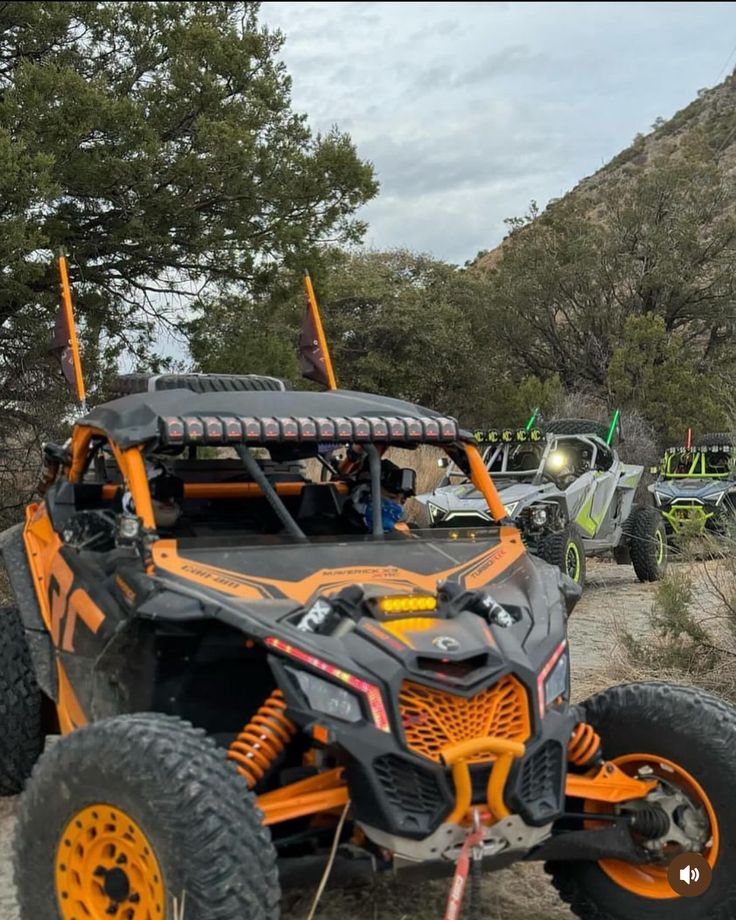 an orange and black buggy is parked on the side of a dirt road with other vehicles in the background